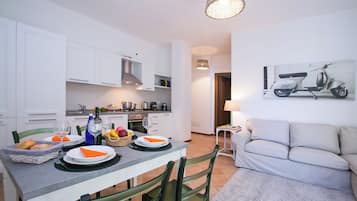 Una cocina moderna con armarios blancos, una mesa de comedor dispuesta con platos y cubiertos, un sofá y una lámpara fijada a la pared.