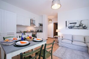 Une cuisine moderne avec des meubles blancs, une table à manger dressée avec des assiettes et des couverts, un canapé et une lampe fixée au mur.
