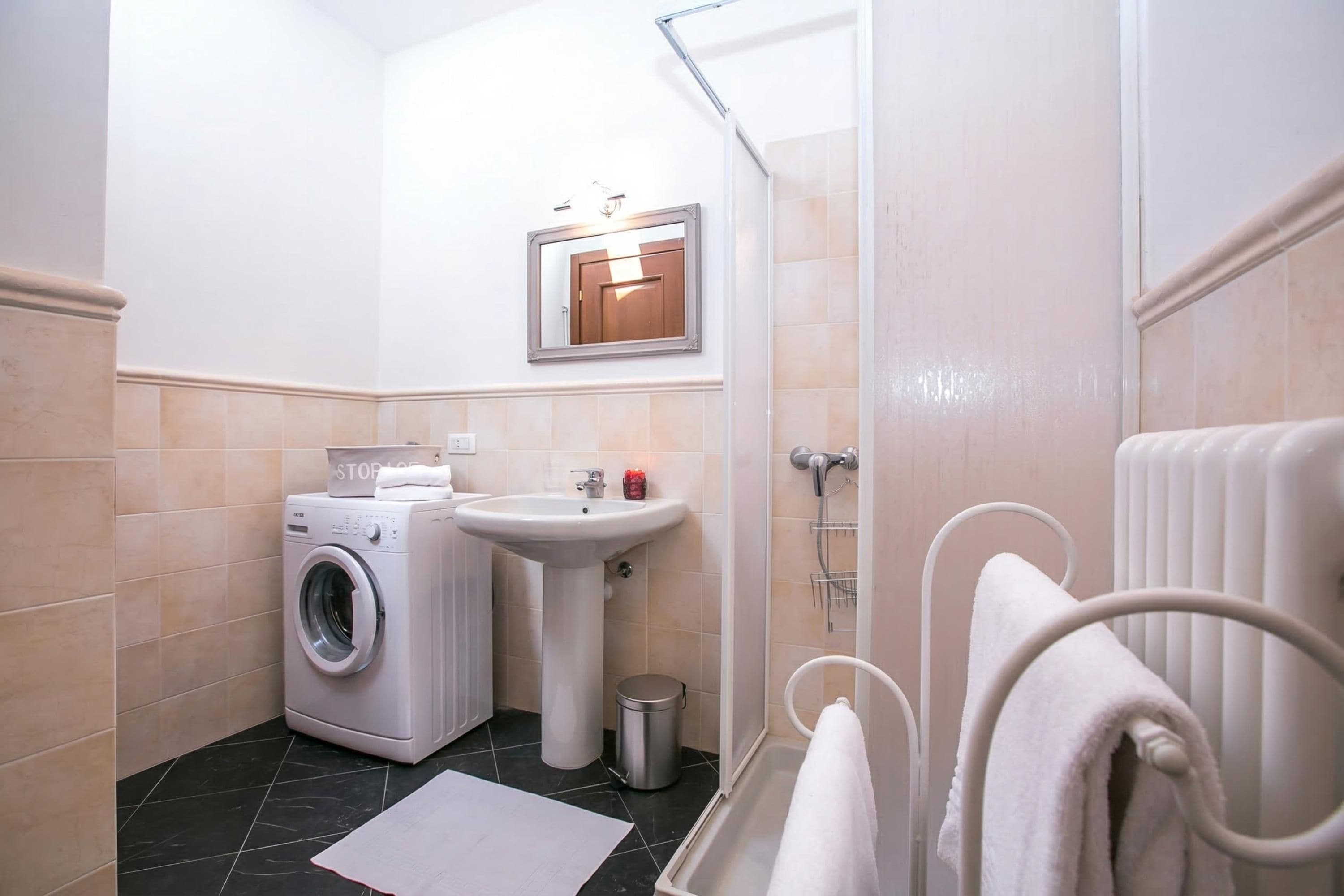 Een kleine badkamer met een wasmachine, wastafel en douche.