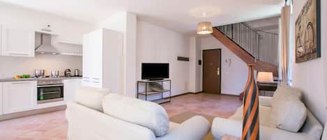 A modern living space with a sofa, a TV, a staircase, and a kitchen area.