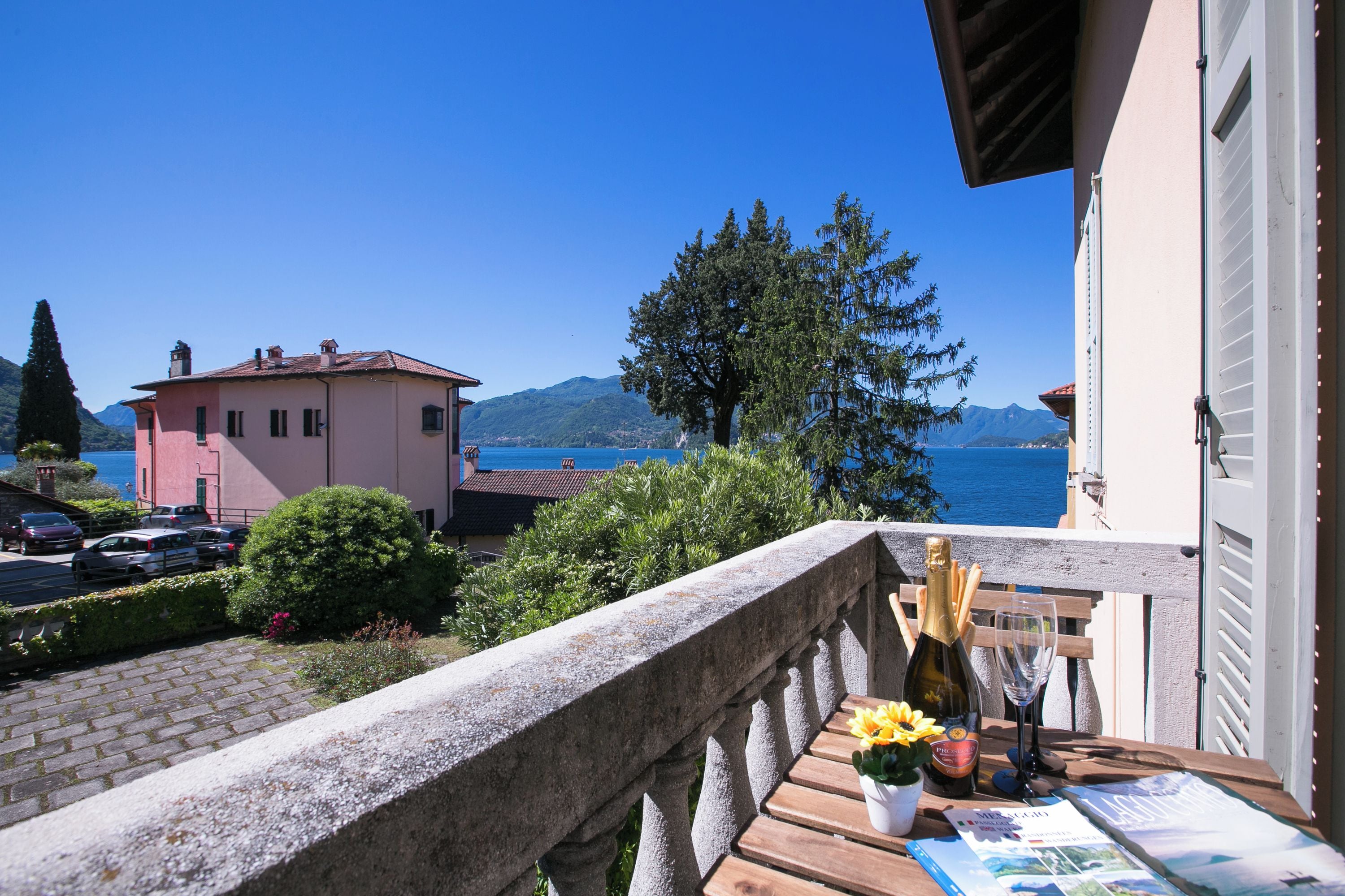 A balcony with a view of the sea and mountains, a wooden table with a bottle of champagne, a glass, and a magazine.