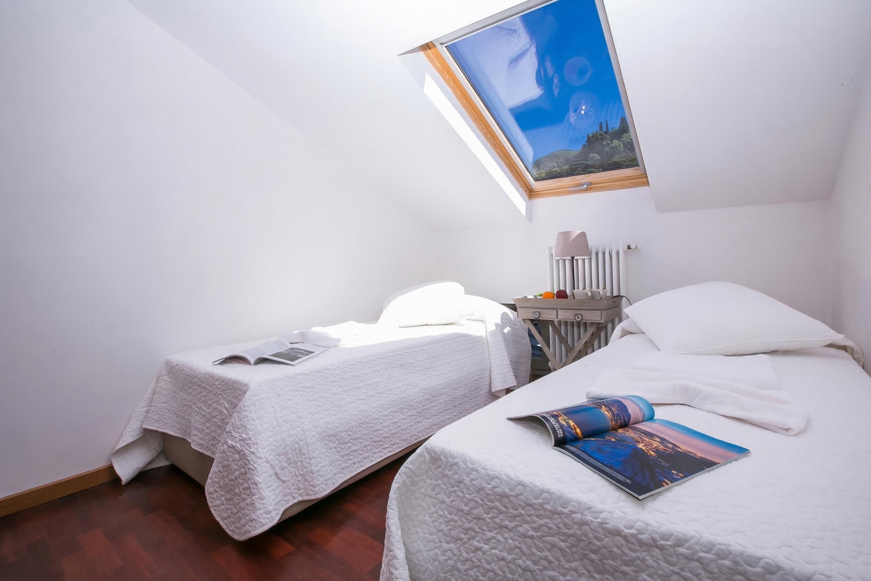 A room with two beds, a skylight, a radiator, and a magazine on the right bed.