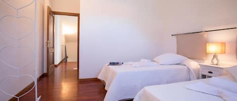 A hotel room with two beds, a nightstand with a lamp, a white radiator, and a wooden floor.