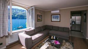 A modern living room with a large window offering a view of a lake and mountains. - Laglio Deluxe (Carate Urio)