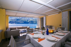 A dining area with a table set for four, overlooking a scenic view of a lake and mountains. - Laglio Deluxe (Carate Urio)