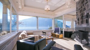 Ein geräumiges Wohnzimmer mit Kamin, großen Fenstern und Blick auf die Berge.
