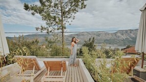 A wooden deck with lounge chairs, a person standing, and a mountainous landscape in the background.
