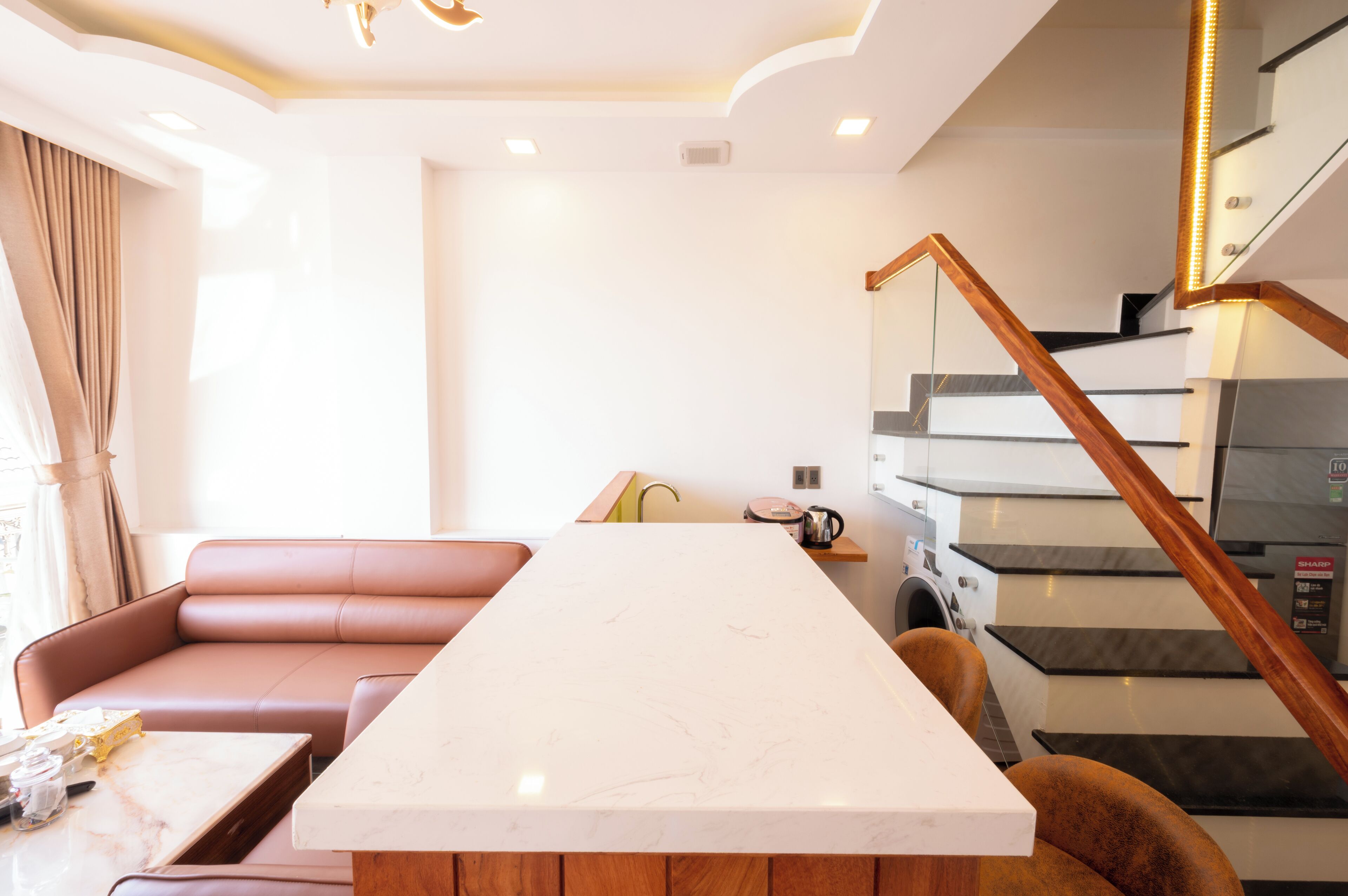 A modern kitchen with a marble countertop, a built-in oven, and a staircase with wooden railings.