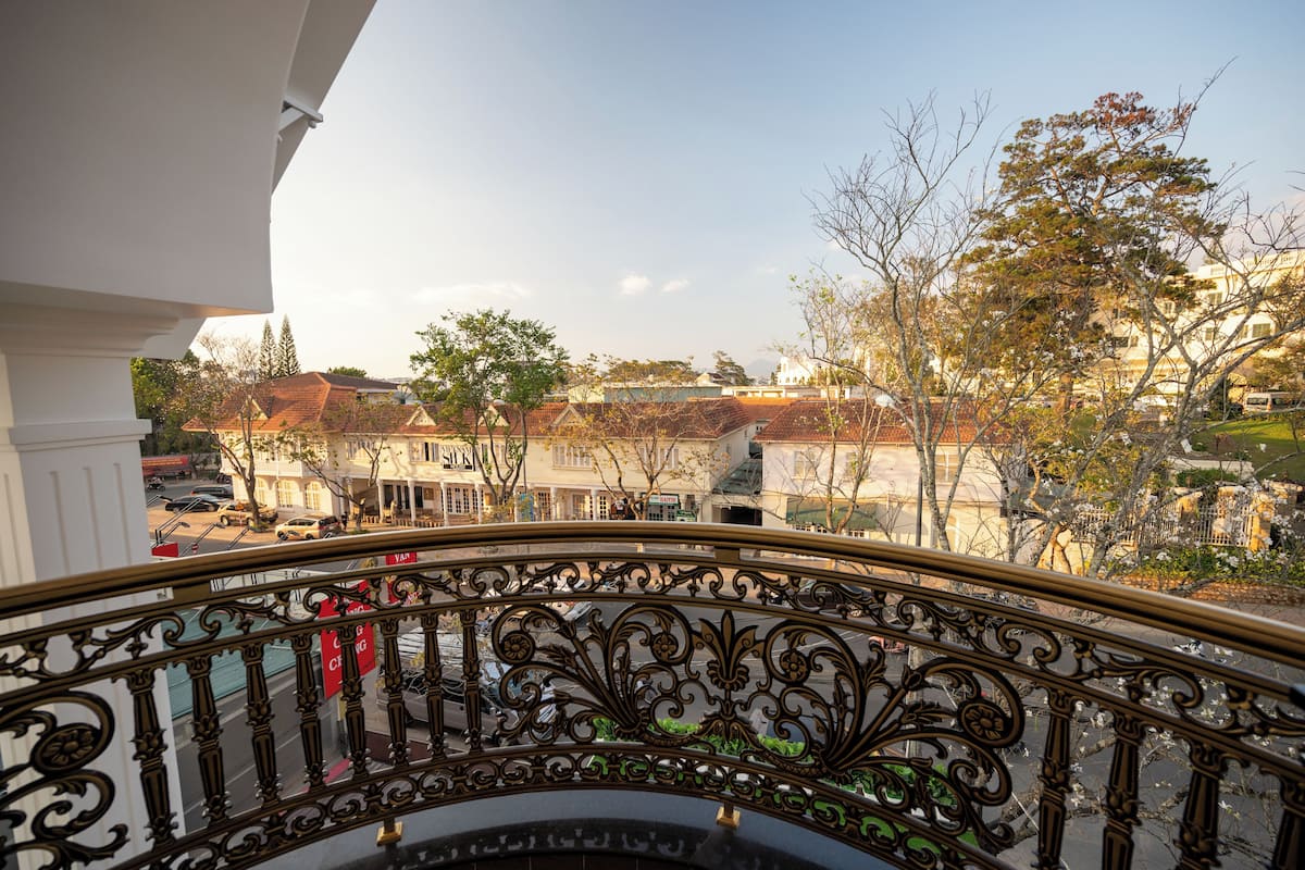 A balcony with ornate iron railings overlooking a residential area with houses and trees.