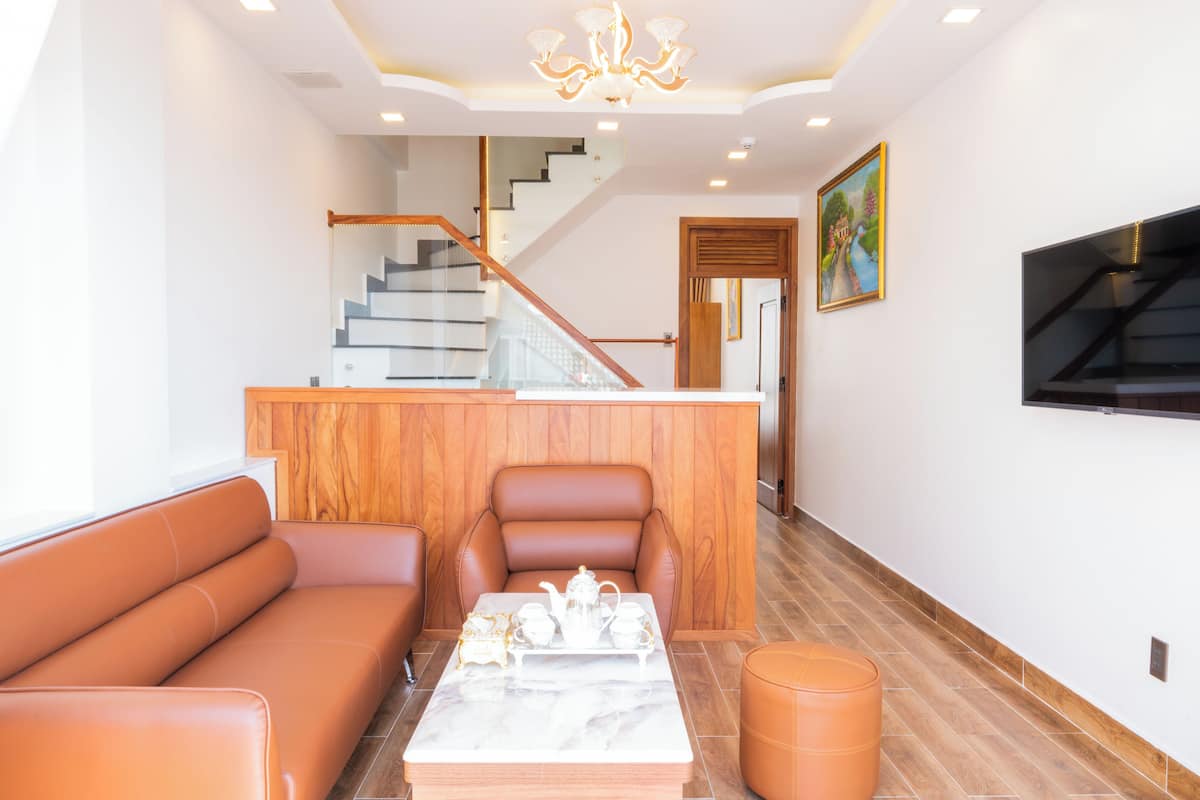 A modern living room with a sofa, a coffee table with tea set, a wooden accent wall, a staircase, and a TV mounted on the wall.