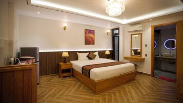 A modern hotel room with a wooden bed, bedside lamps, a chandelier, a painting on the wall, and a bathroom with a mirror and sink.