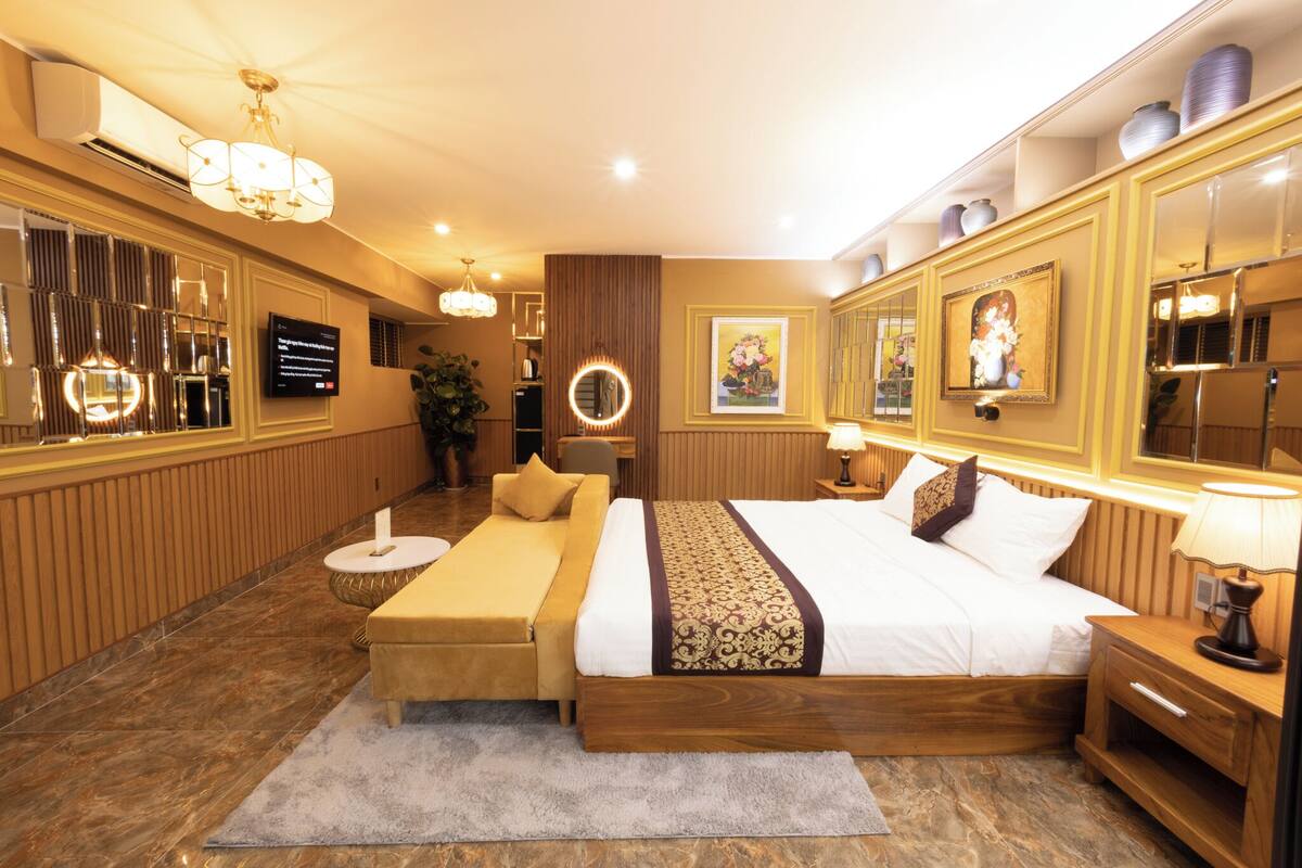A hotel room with a large bed, a bedside table, a nightstand, a TV, a mirror, and a decorative wall panel.