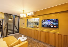 A hotel lobby with a large TV screen displaying a sports channel, a staircase leading to another floor, and a yellow sofa.