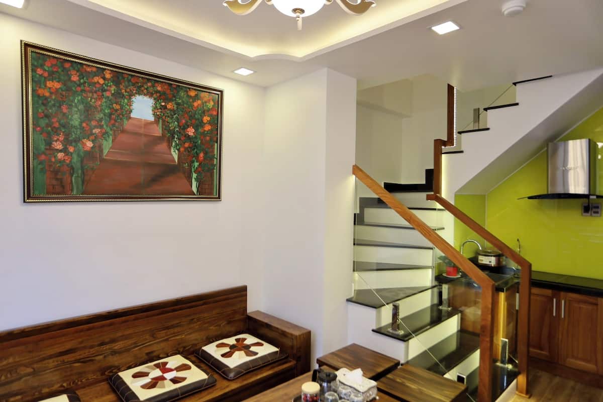 A modern living room with a wooden bench, a glass staircase, and a green accent wall.