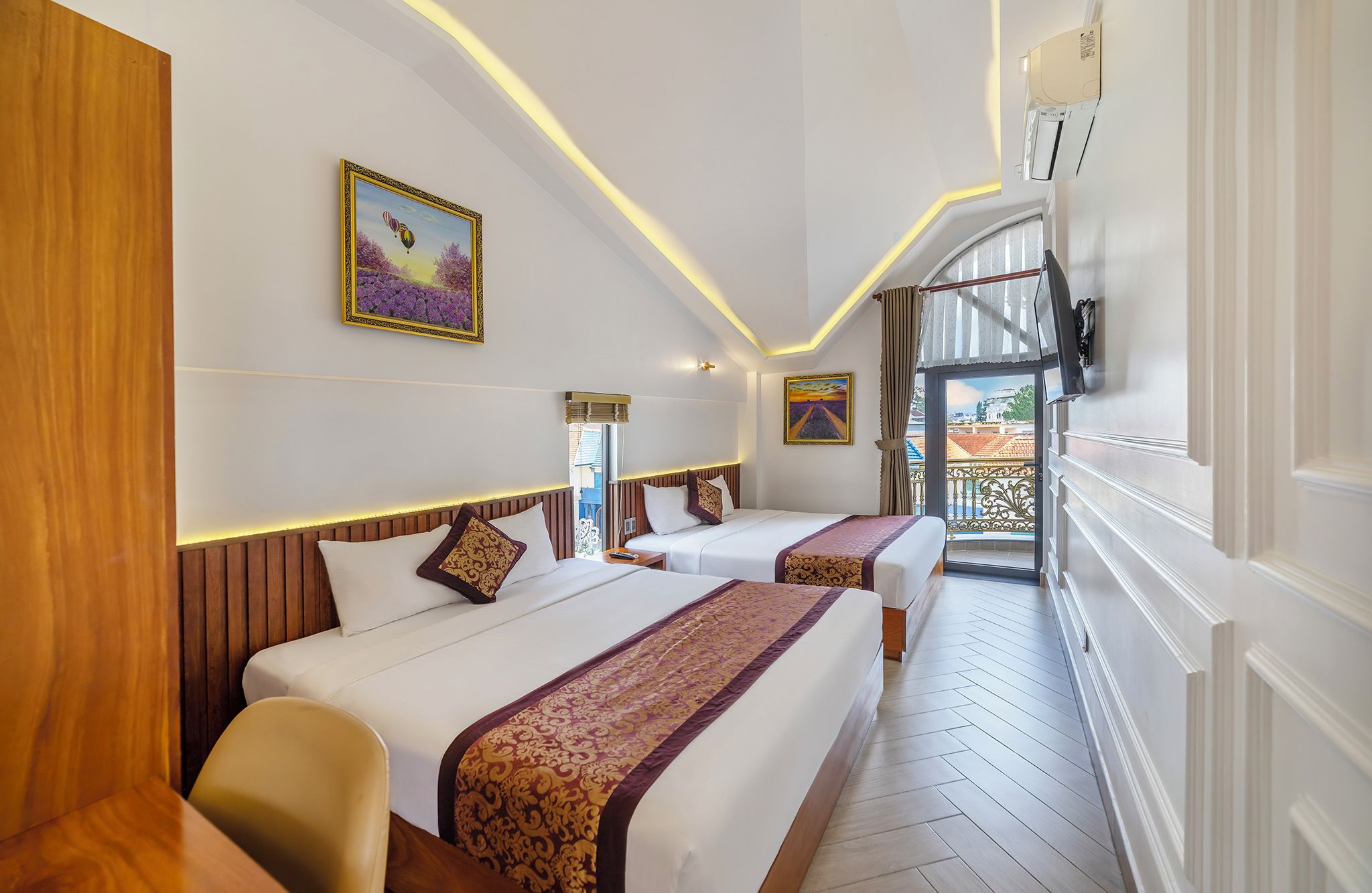 A hotel room with two beds, a wooden headboard, a painting, a ceiling light, and a view of the outside.