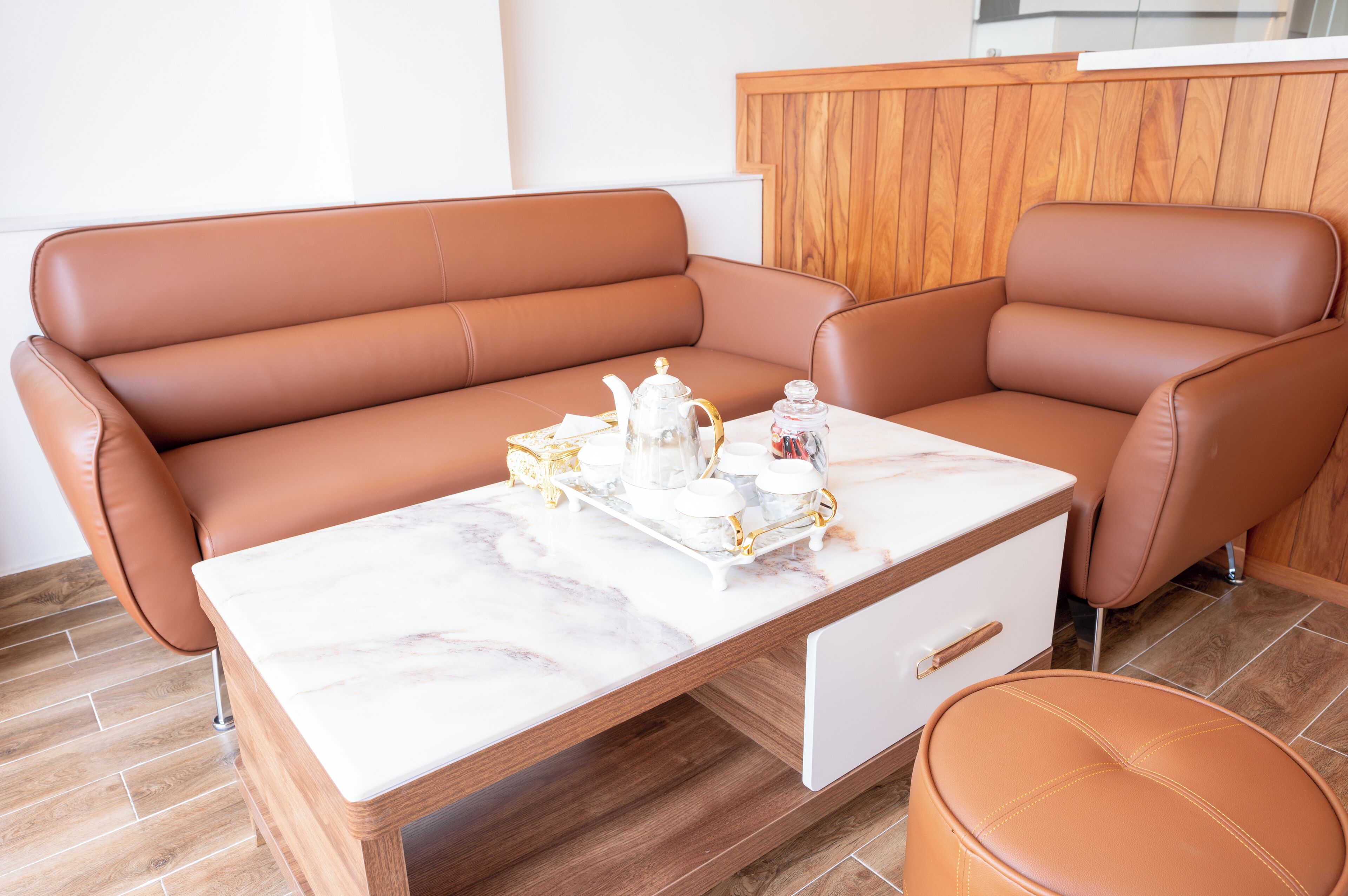Een moderne woonkamer met een bruine leren bank, een marmeren bijzettafeltje en een bijpassend pouf.