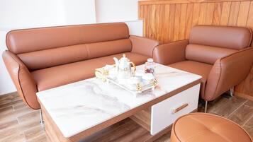 Een moderne woonkamer met een bruine leren bank, een marmeren bijzettafeltje en een bijpassend pouf.