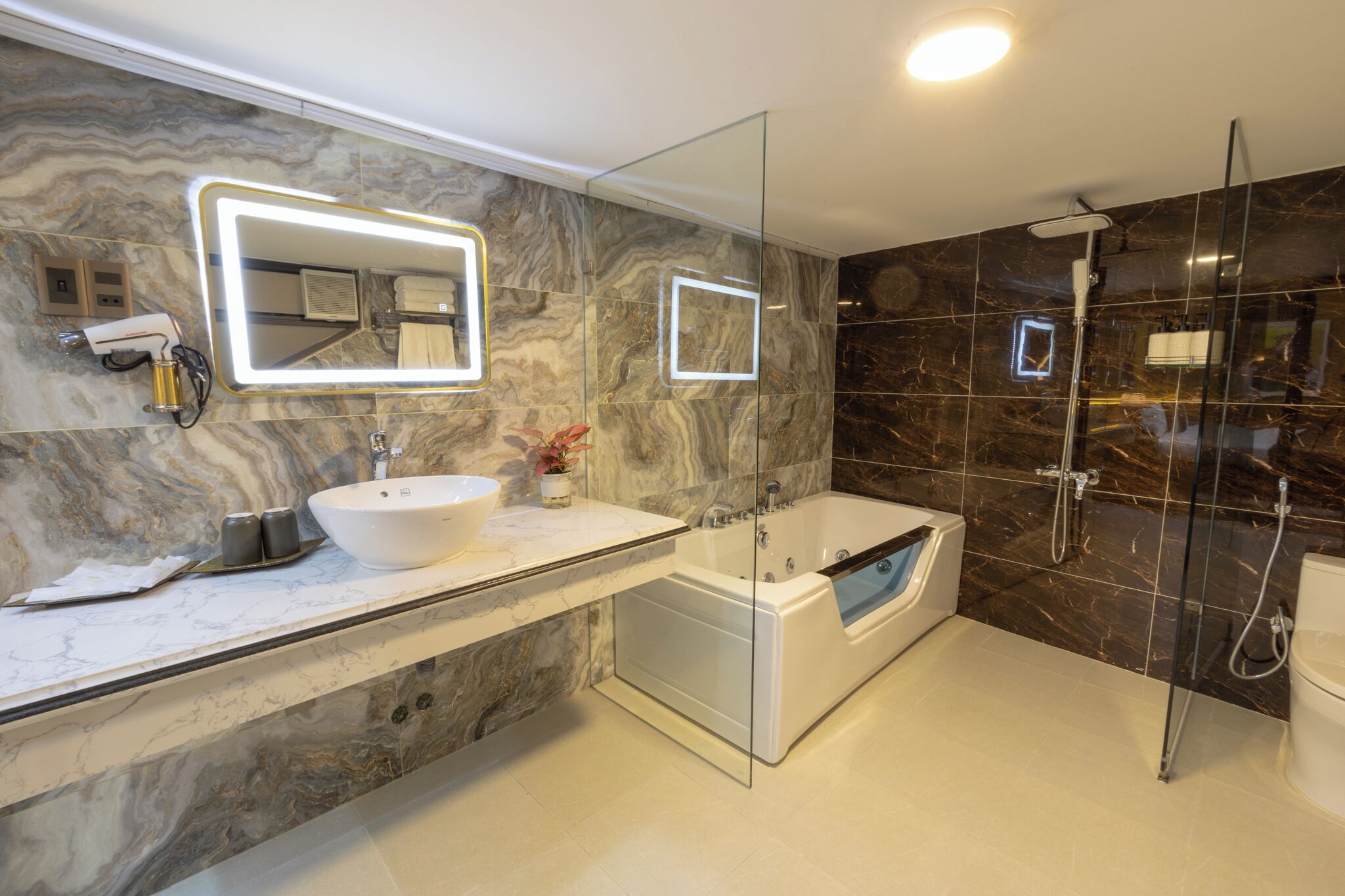 Un baño moderno con tocador de mármol, un espejo grande, una bañera y zona de ducha con mampara de vidrio.