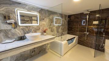 Un baño moderno con tocador de mármol, un espejo grande, una bañera y zona de ducha con mampara de vidrio.