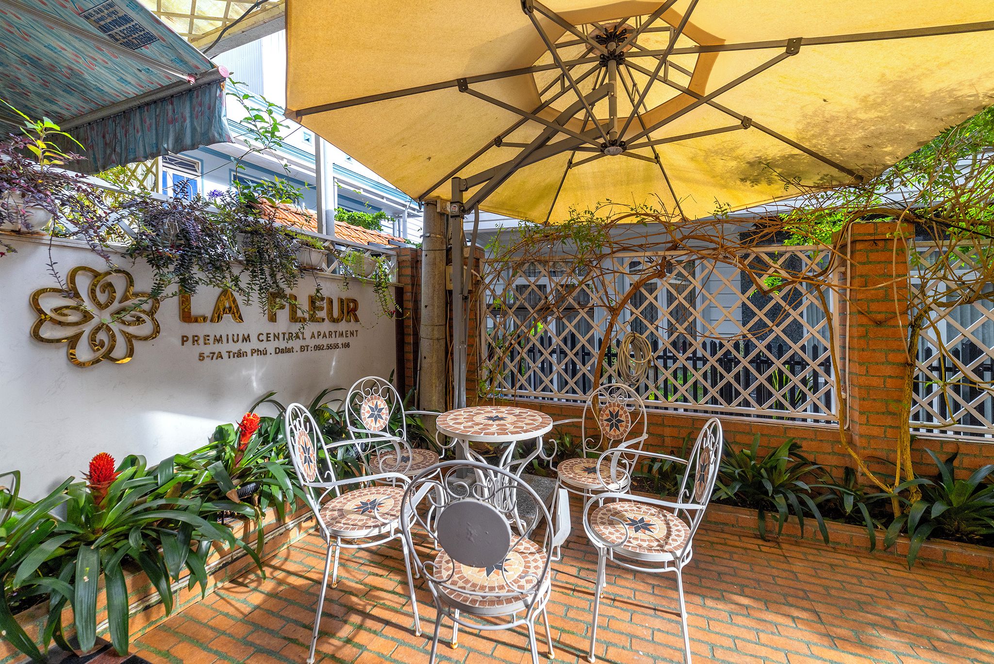 A patio area with outdoor seating, a decorative wall with a flower design, and a yellow umbrella providing shade.