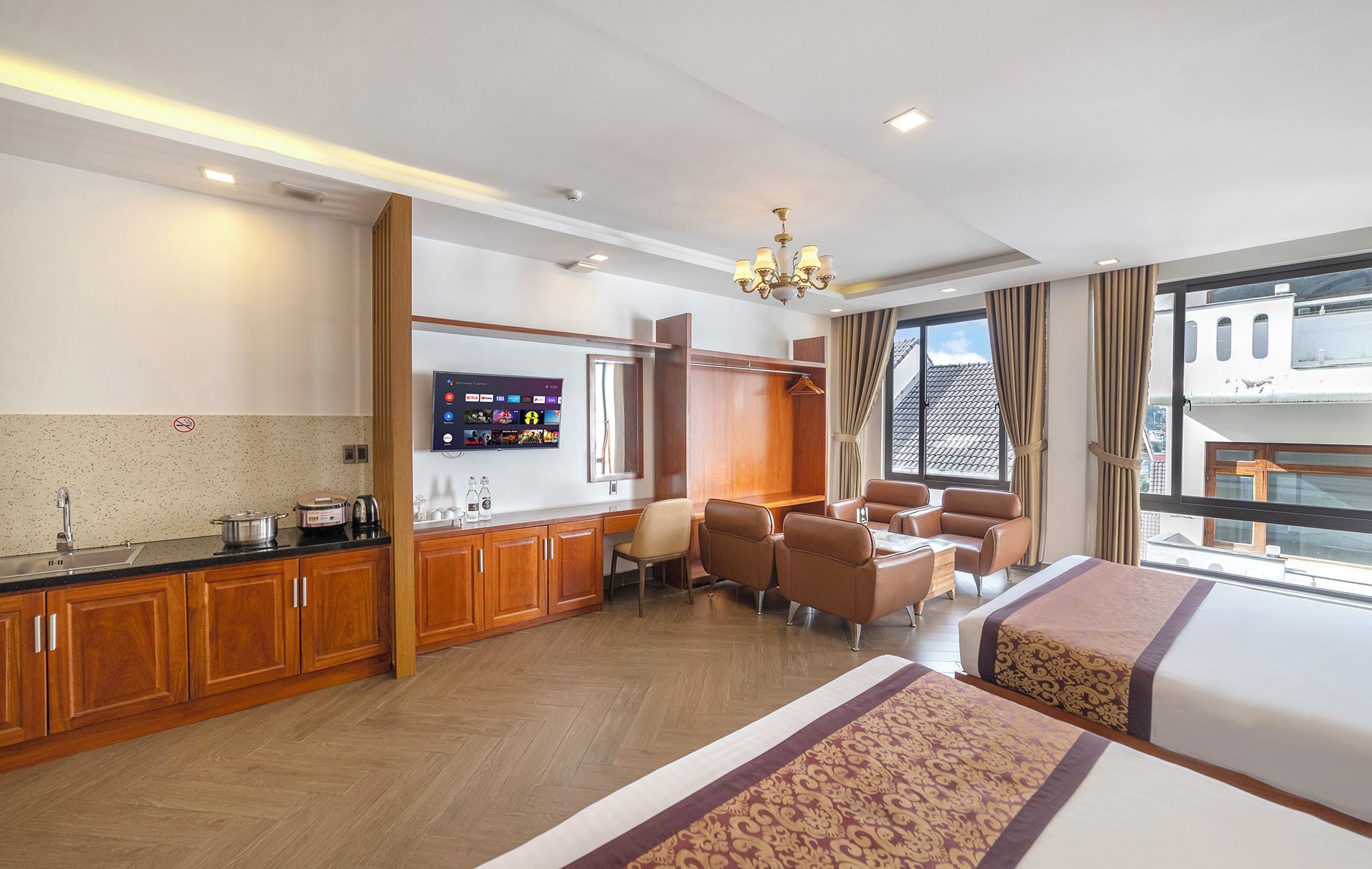 A hotel room with a kitchenette, a TV, a seating area with chairs, a bed, and a large window with curtains.