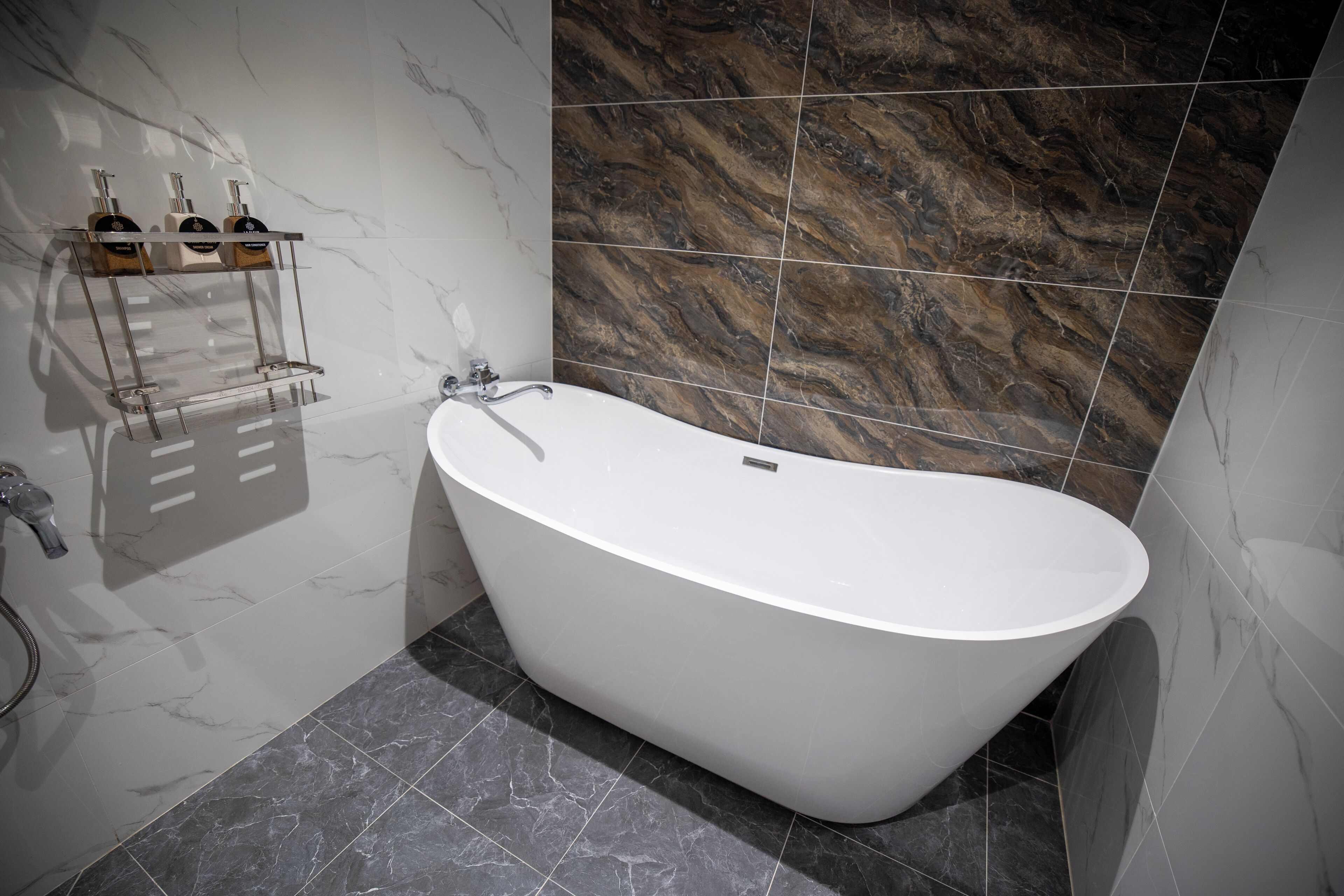 A modern bathroom with a freestanding bathtub, marble walls, and a built-in shelf with toiletries.