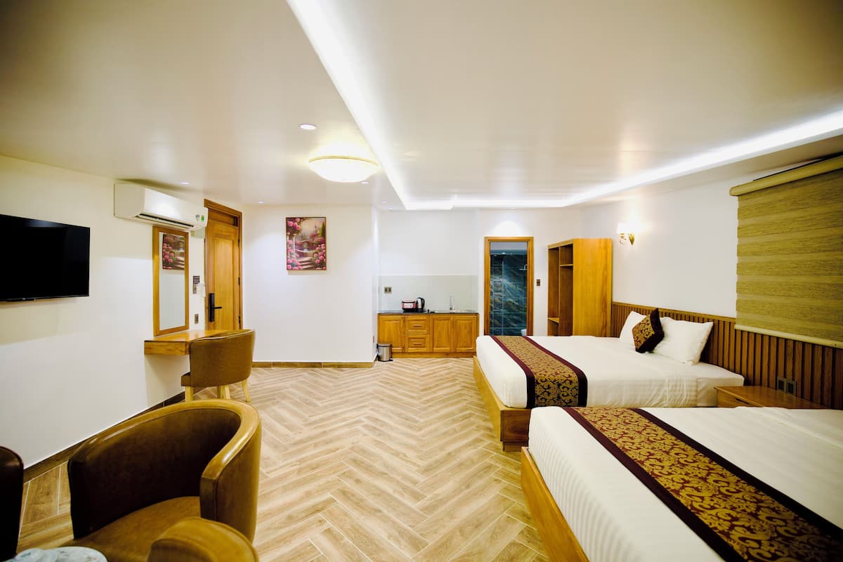 A hotel room with two beds, a wooden chair, a desk, a TV, and a kitchenette.