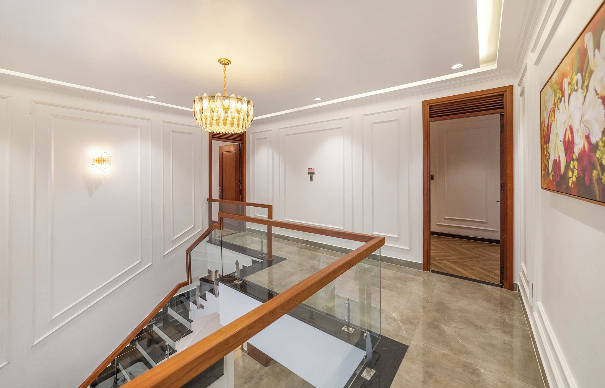 A modern interior with a glass staircase, a chandelier, and a painting on the wall.