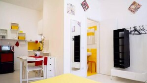 Une pièce de taille modeste comprenant un lit, un bureau, une chaise, une armoire et une petite kitchenette.