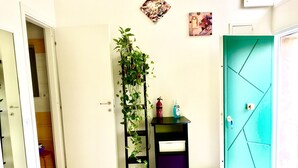Une pièce avec une porte blanche, une porte de couleur turquoise, une petite table noire avec une plante et un extincteur.