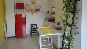 Une cuisine de taille réduite avec un réfrigérateur rouge, une petite chaise noire et une table blanche avec des assiettes jaunes.