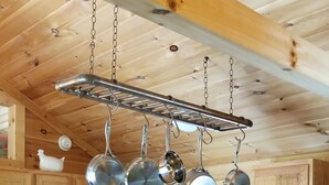 A kitchen with wooden cabinets, a stainless steel range hood, a microwave, a stove, and hanging pots. - Homestead Cabin with hot tub                                                     (Strawberry Plains)