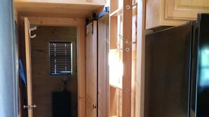 A wooden interior with a black refrigerator, wooden shelves, and a window with blinds. - Homestead Cabin with hot tub                                                     (Strawberry Plains)