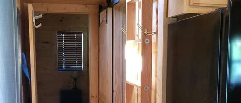 A wooden interior with a black refrigerator, wooden shelves, and a window with blinds.