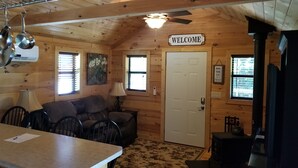A cozy cabin interior with a wooden interior, a couch, a table, a stove, and a 'WELCOME' sign. - Homestead Cabin with hot tub                                                     (Strawberry Plains)