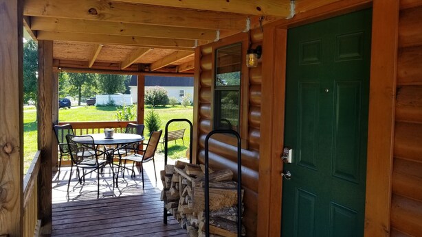 A wooden cabin with a covered porch, a dining table with chairs, and a green door. - Homestead Cabin with hot tub                                                     (Strawberry Plains)