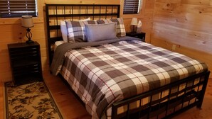 A wooden-framed bed with a plaid bedspread, a nightstand with a lamp, and a floral-patterned rug. - Homestead Cabin with hot tub                                                     (Strawberry Plains)