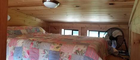 Un dormitorio con techo de madera, una cama con colcha floral, un ventilador de techo y una ventana.