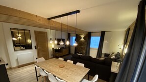 Ein modernes Wohnzimmer mit einem Holzesstisch, weißen Stühlen, einem schwarzen Sofa und einer Wand als Steinakzent.
