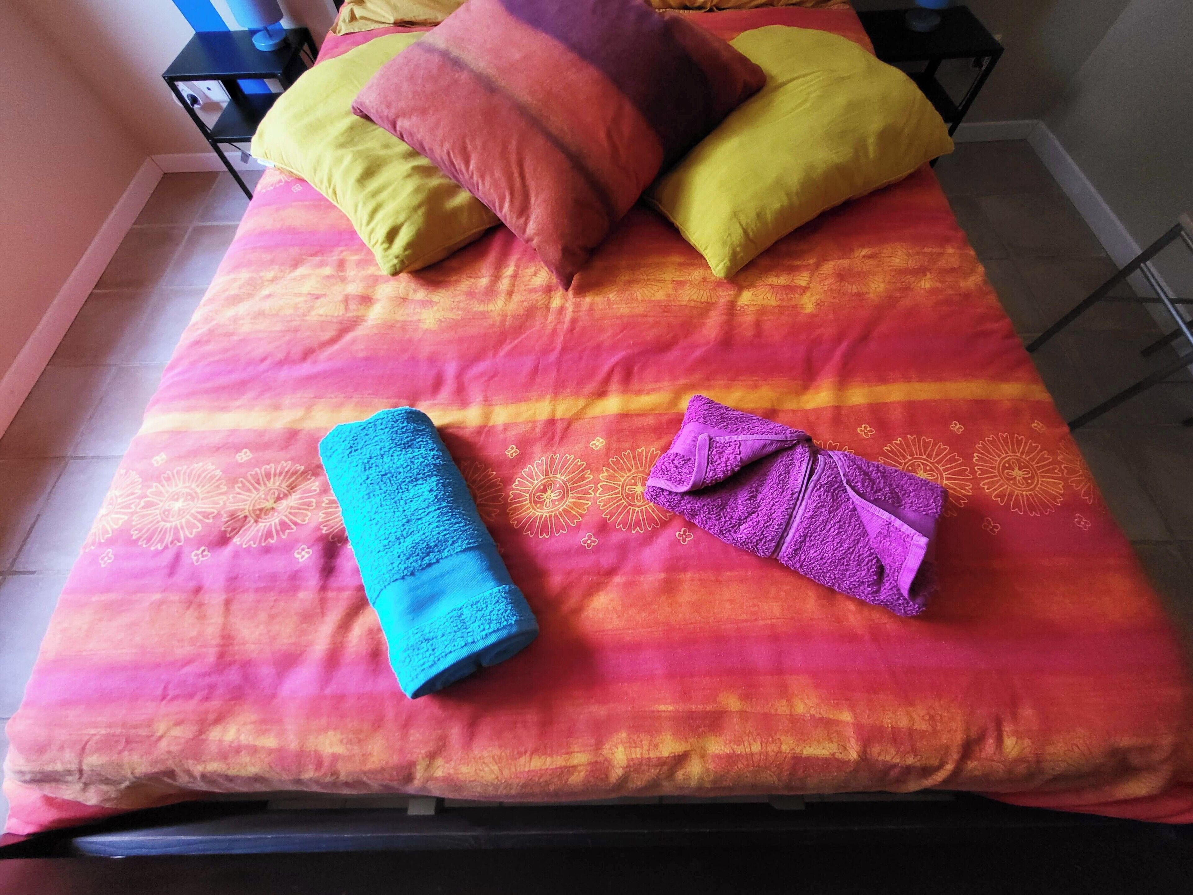 Un lit avec une couvre-lit aux couleurs vives et deux serviettes enroulées.