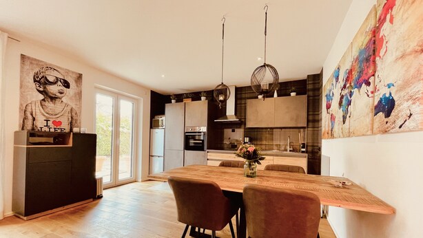Une cuisine moderne avec un coin repas, comprenant une table en bois, des chaises et des luminaires suspendus.