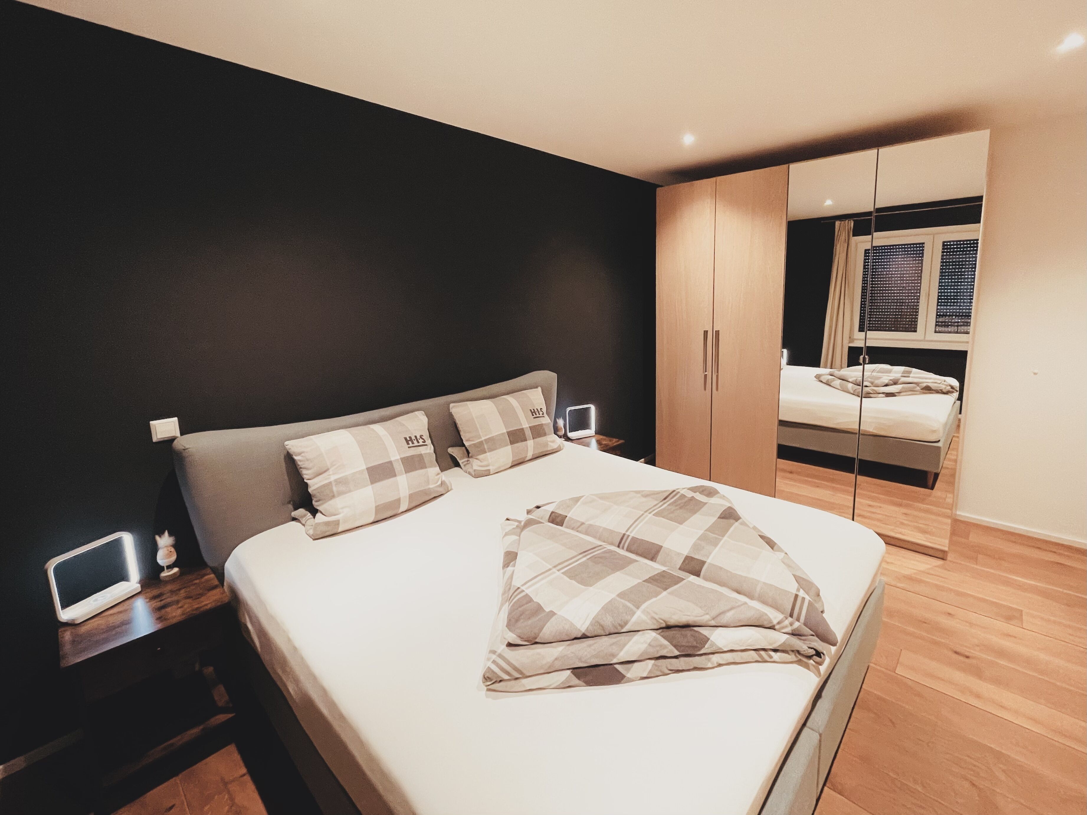 Ein modernes Schlafzimmer mit einem Bett, Nachttischen, einem Spiegel und einem Kleiderschrank.