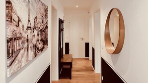 Un couloir doté d’un plancher en bois, d’un banc, d’un grand tableau représentant un paysage urbain et d’un miroir rond accroché au mur.