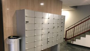 Een rij metalen lockers met aparte vakken, een prullenbak en een trap met een rode leuning.