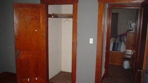 A room with a wooden door, a closet with a hanging rod, and a bed with a headboard.