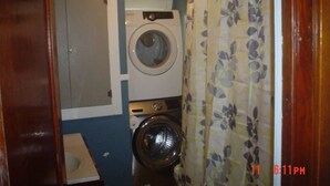A compact laundry room with a washing machine and dryer, a small sink, and a shower curtain.