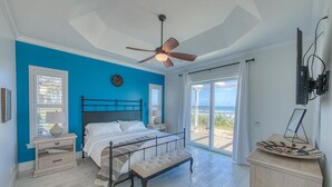 A bedroom with a bed, a nightstand, a bench, a ceiling fan, and a view of the outdoors.
