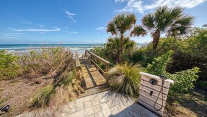 A wooden boardwalk leading to a beach with palm trees and a clear sky.
