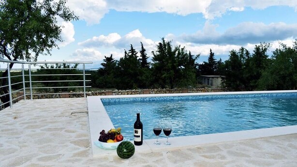 Una piscina con cubierta de piedra, rodeada de árboles y una valla metálica.