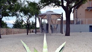 Un espacio de estar al aire libre cubierto con una mesa y sillas, rodeado de árboles y un muro de piedra.